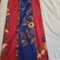 A bolt of cloth sitting on a bedspread. The cloth is crimson and navy blue, and covered in multicoloured flowers.